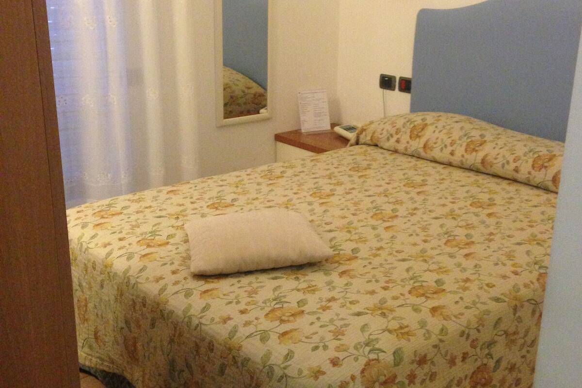 Un dormitorio con colcha estampada, mesita de noche con lámpara y espejo en la pared.