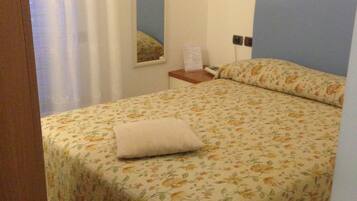 A bedroom with a floral bedspread, a nightstand with a lamp, and a mirror on the wall.