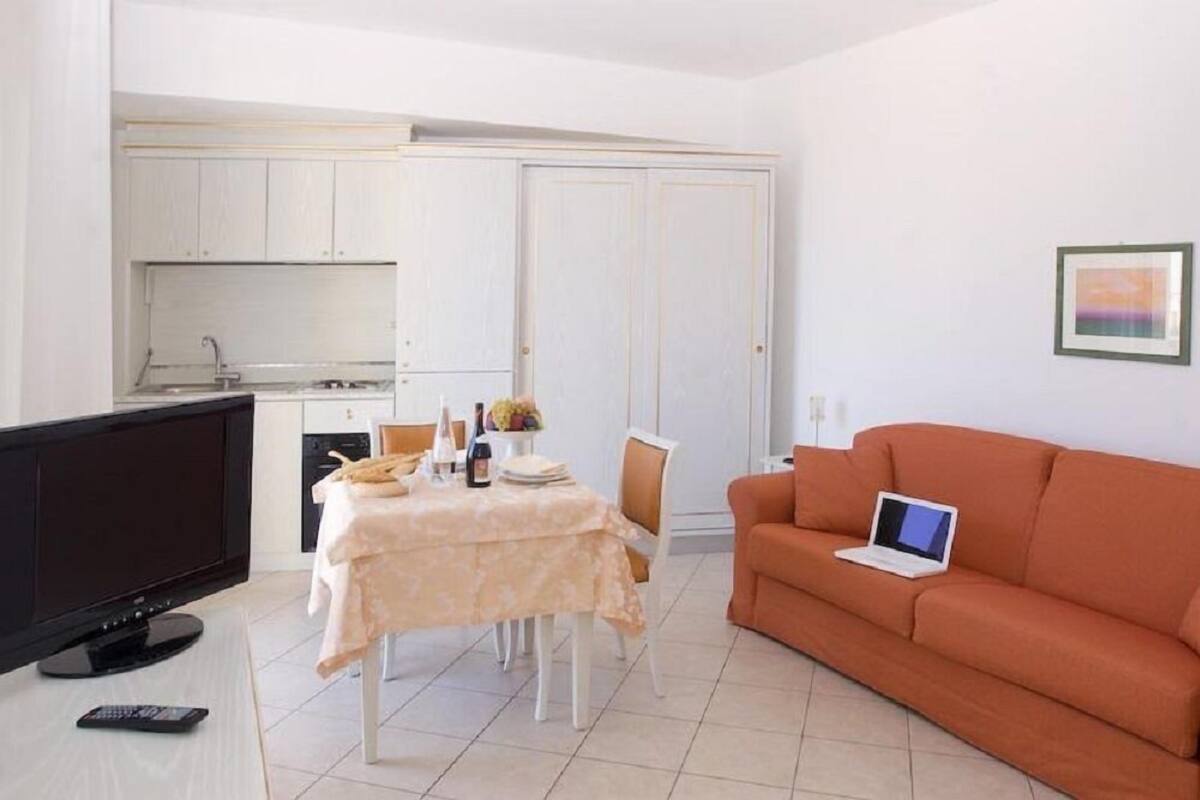Un espacio habitable compacto con comedor, kitchenette y un sofá con una computadora portátil.