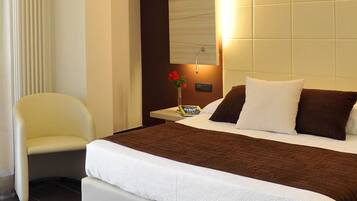 A hotel room with a bed, a chair, a bedside table with a lamp, and a nightstand with a phone.