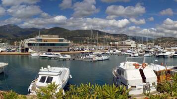 A marina with multiple boats docked, a red building, and a mountainous backdrop.