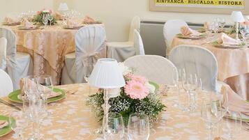 A banquet hall with round tables, each set with white chairs, green plates, and pink napkins.