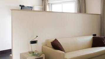 A hotel room with a beige sofa, a small side table, a lamp, and two framed artworks on the wall.