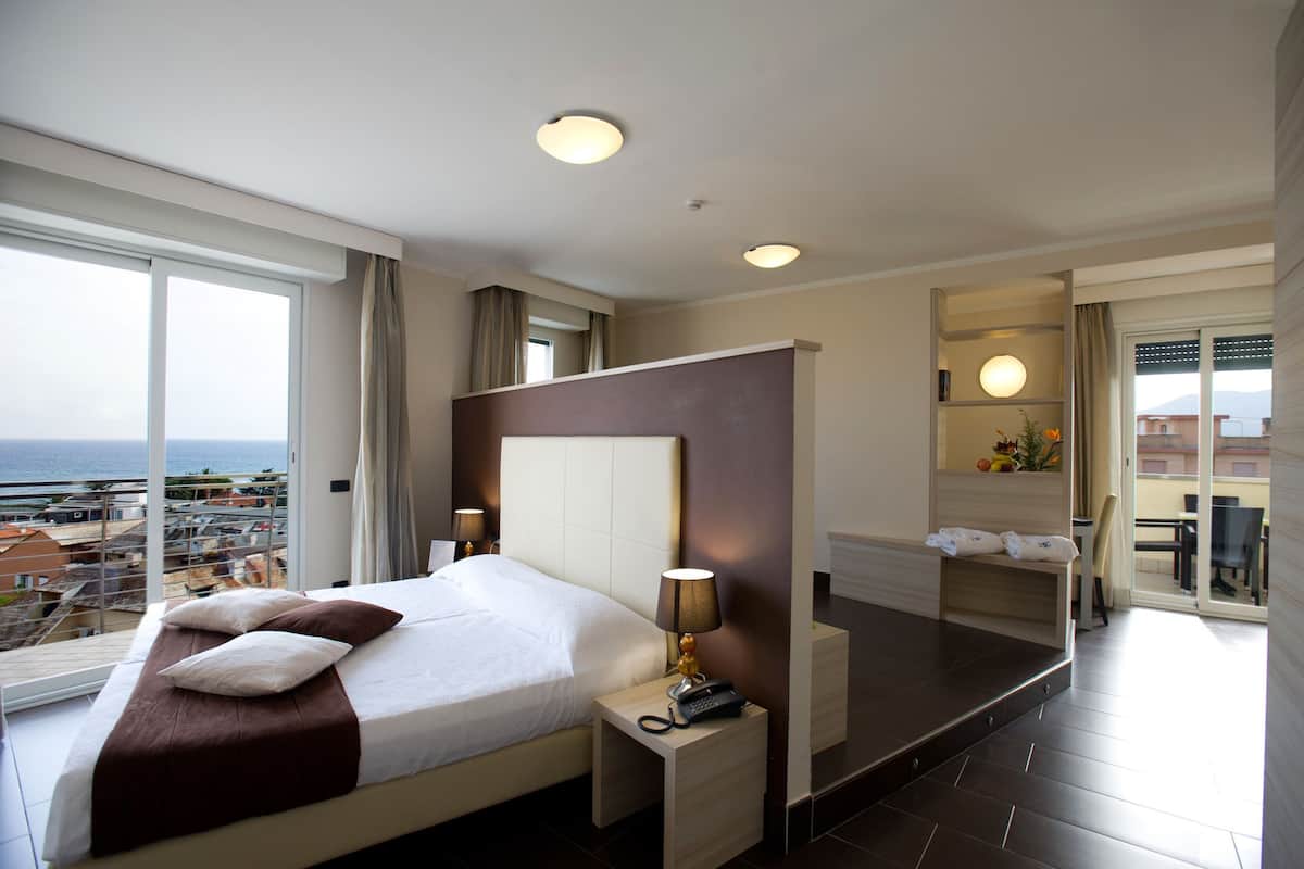 Habitación de hotel con una cama grande, lámparas de noche, un teléfono y vistas a la ciudad y al mar.