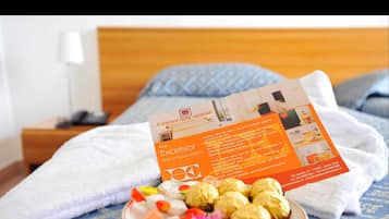 A hotel room with a bed, a bedside table, and a plate with food items.