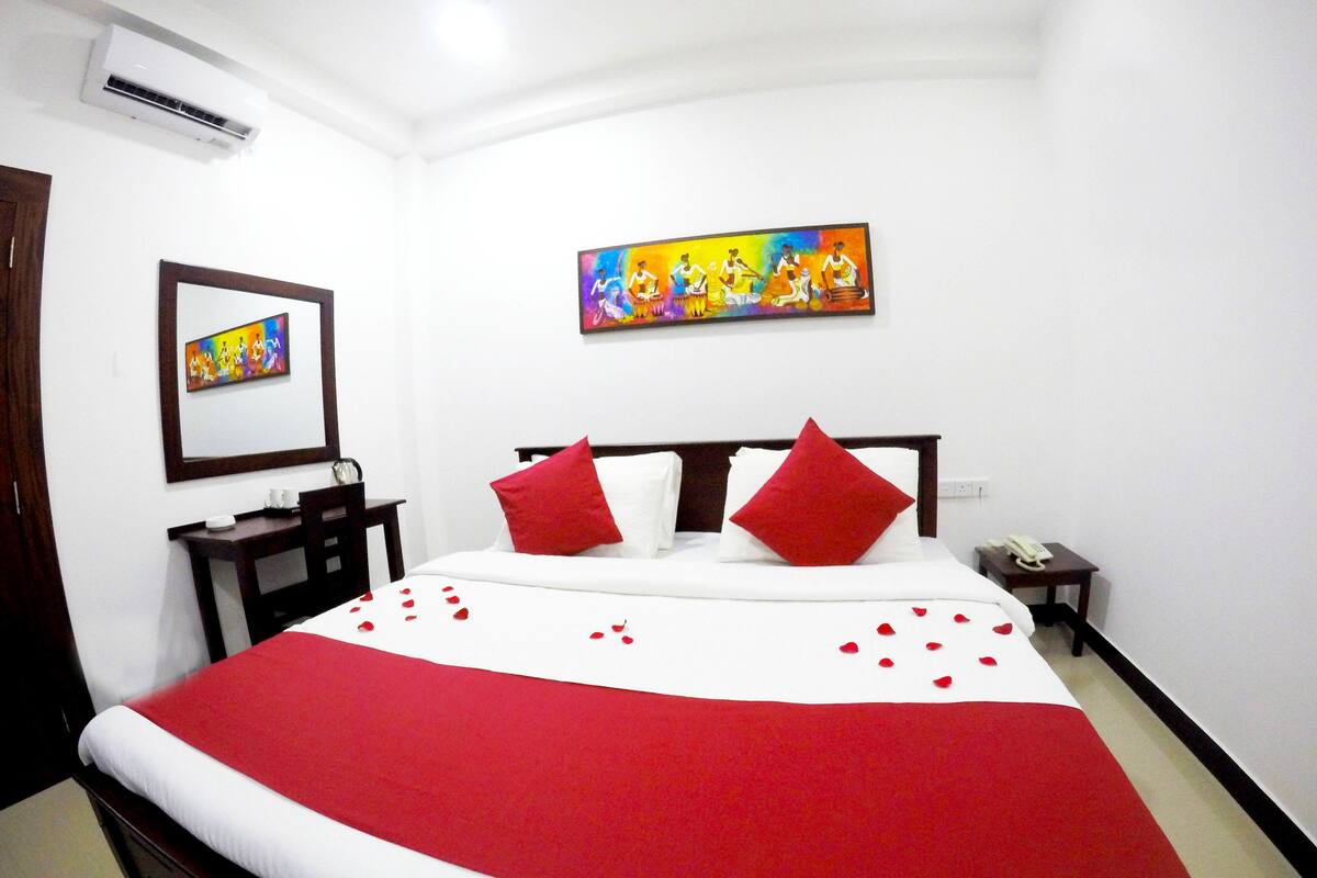 Una habitación de hotel con cama, mesita de noche, aire acondicionado de pared y dos cuadros.