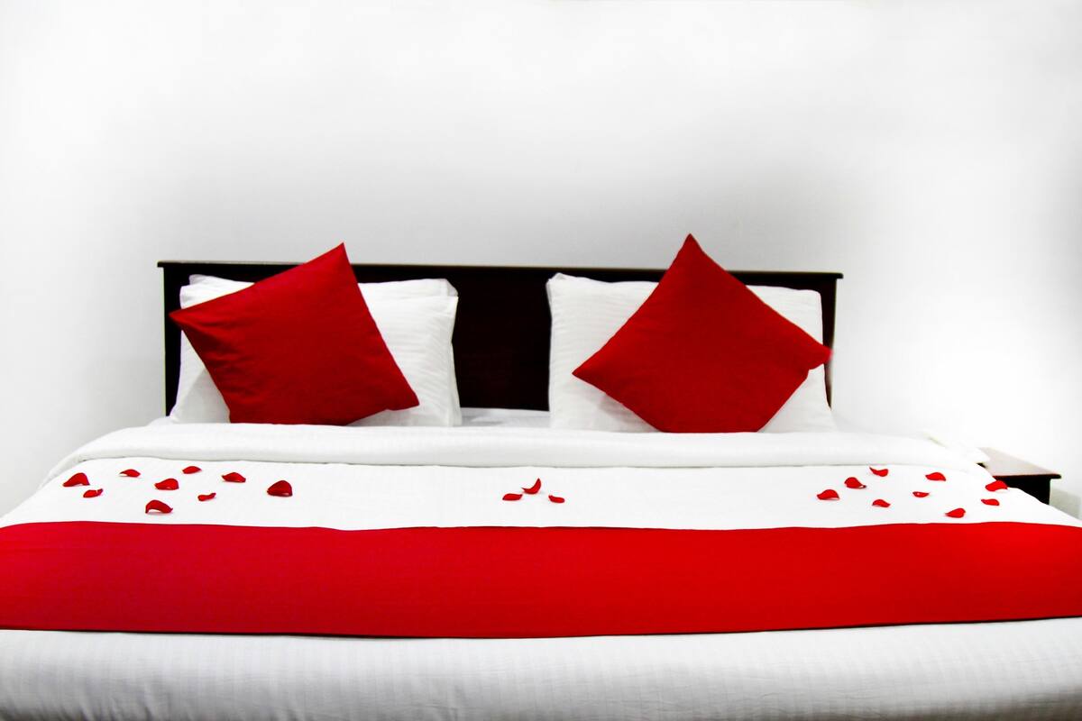 Una cama con ropa de cama blanca y detalles en rojo, incluyendo almohadas y una colcha.