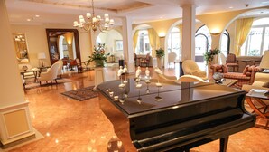 A grand piano in a spacious, elegantly furnished living area with high ceilings, chandeliers, and arched windows. - Delta Resort Apartments (Ascona)
