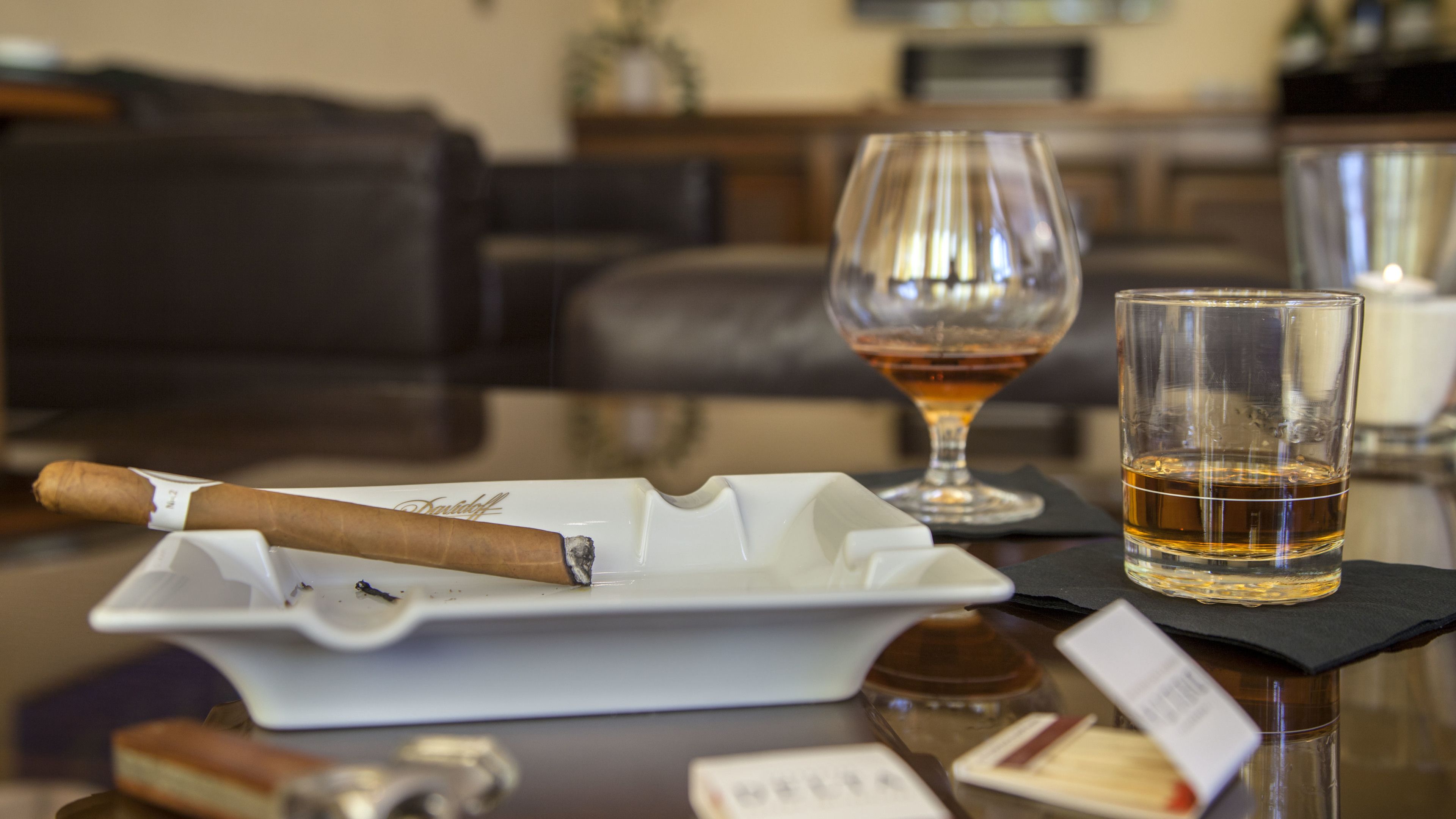 A cigar on a tray, a glass of whiskey, and a glass of water on a table.