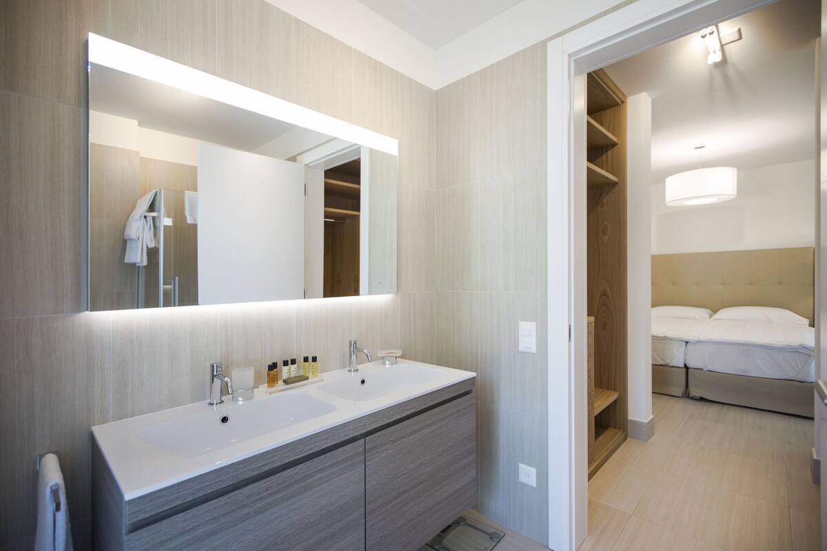 Une salle de bain moderne avec un meuble-lavabo à deux vasques, un grand miroir et un dressing.