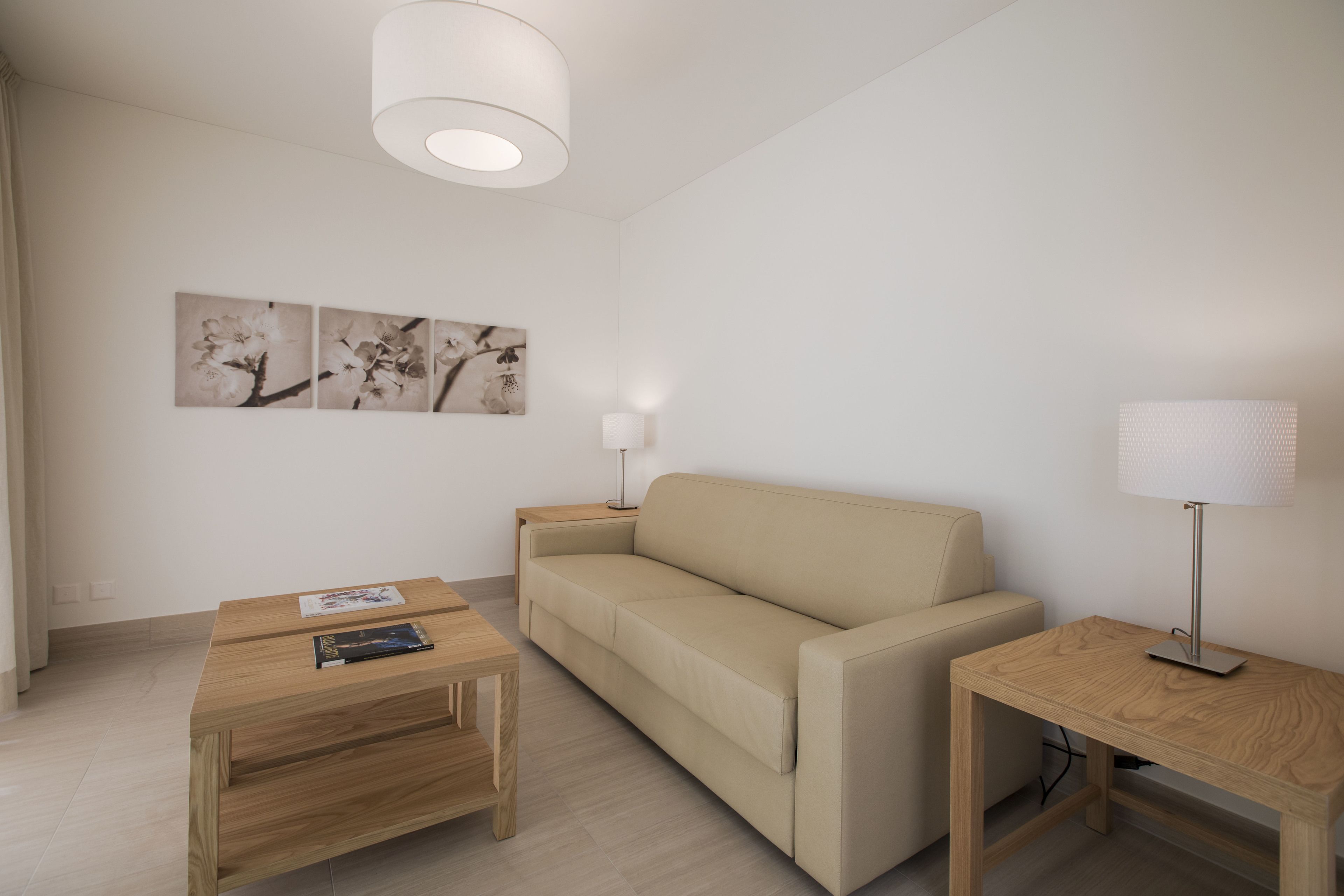 A modern living room with a beige sofa, a wooden coffee table, a side table with a lamp, and wall art.