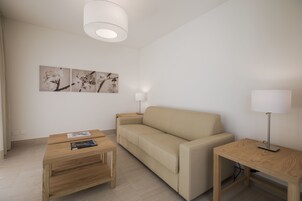 Una sala de estar moderna con un sofá color beige, una mesa de centro de madera, una mesita de noche con lámpara y decoración en la pared.