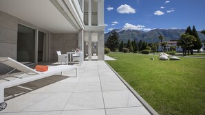 A modern outdoor area with a pool, lounge chairs, and a view of mountains. - Delta Resort Apartments (Ascona)