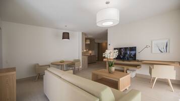 Una sala moderna con sofá, mesa de centro, televisor y zona de cocina.