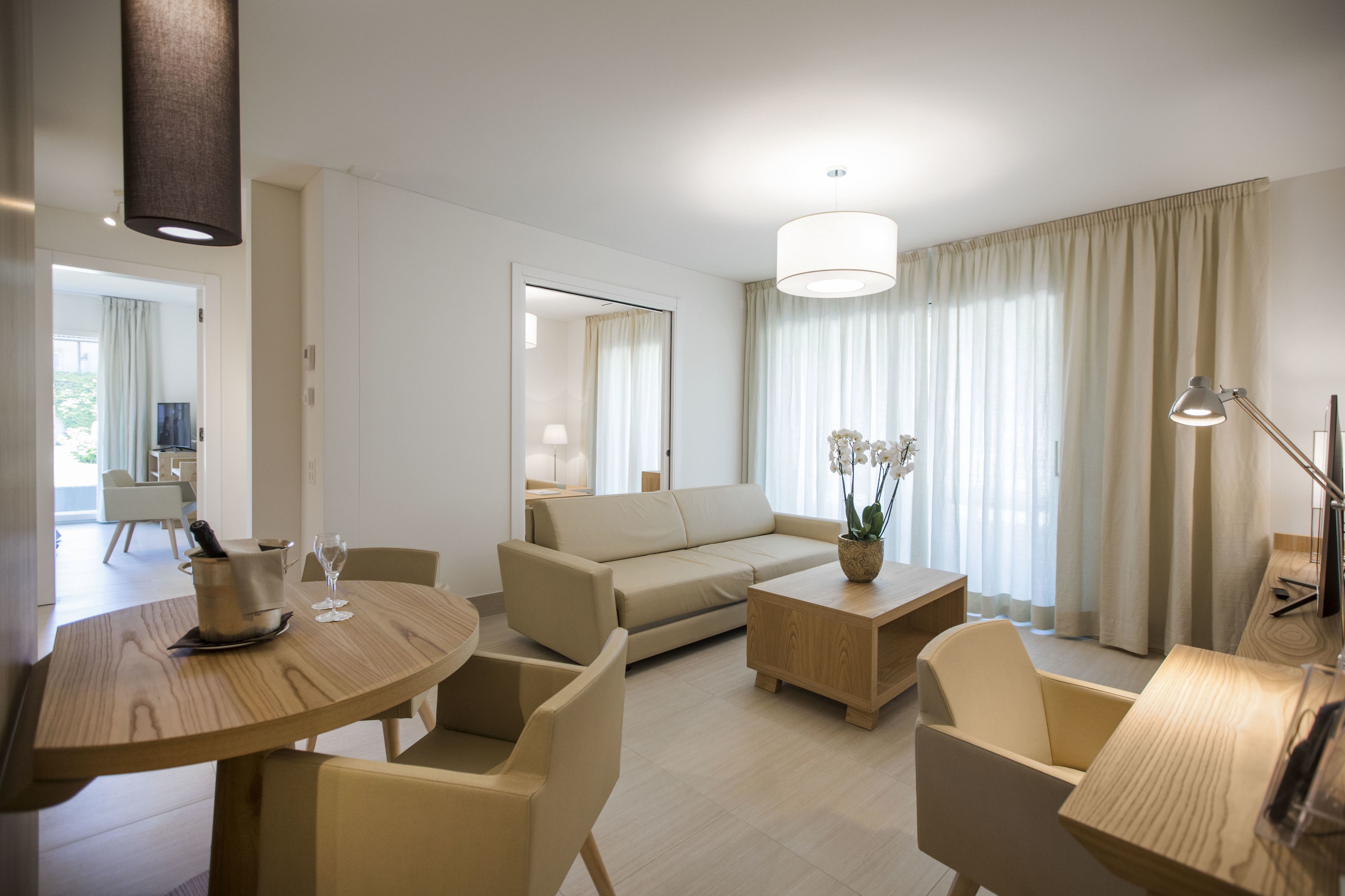 Ein modernes Hotelzimmer mit Wohnbereich, einem Esstisch, einer Couch und einem kleinen Beistelltisch mit Lampe.