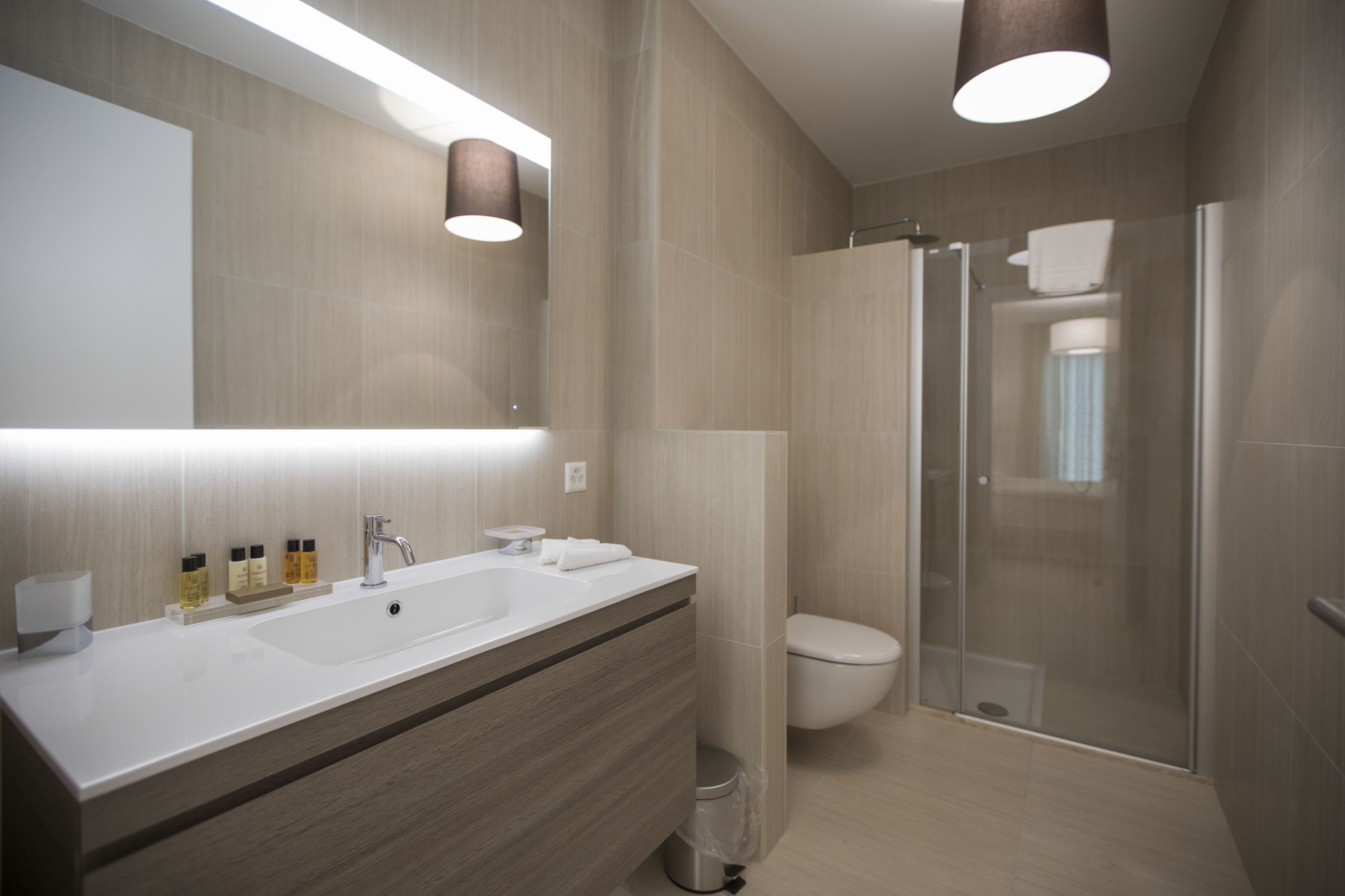 Une salle de bain moderne dotée d’un grand miroir, de deux vasques, de toilettes et d’une douche à parois de verre.