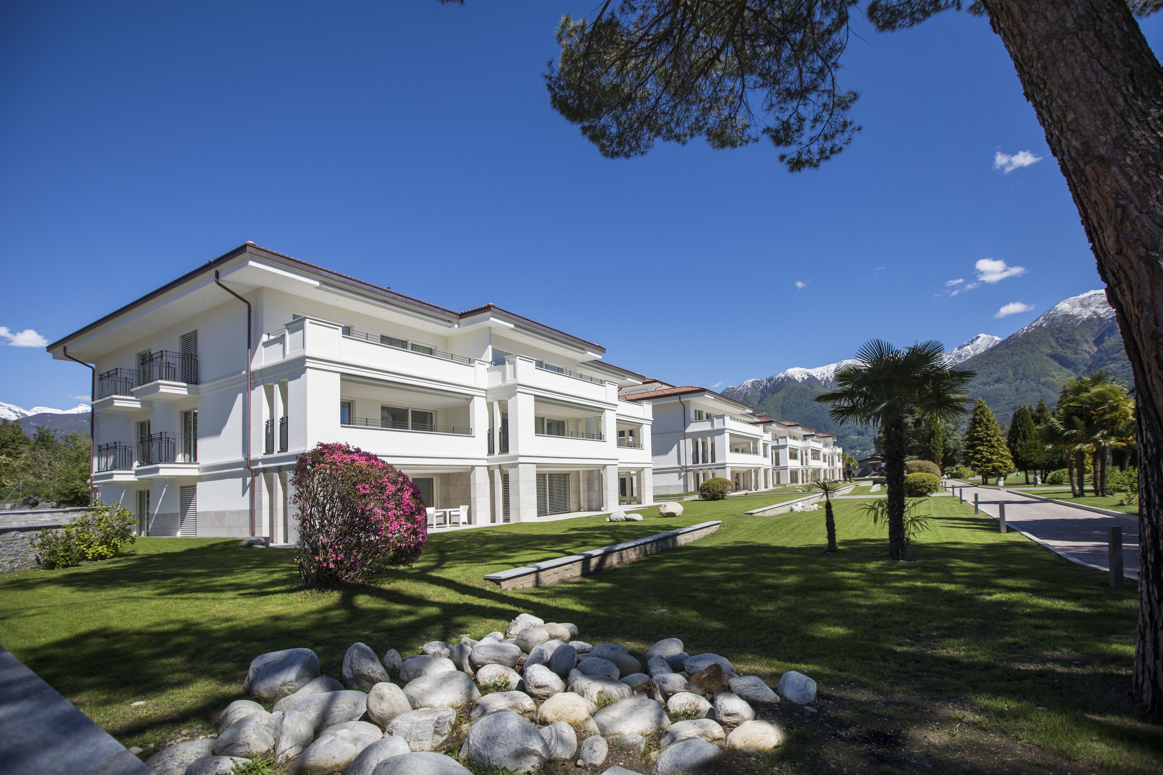 A multi-story hotel with balconies, a well-maintained lawn, and a mountainous backdrop.