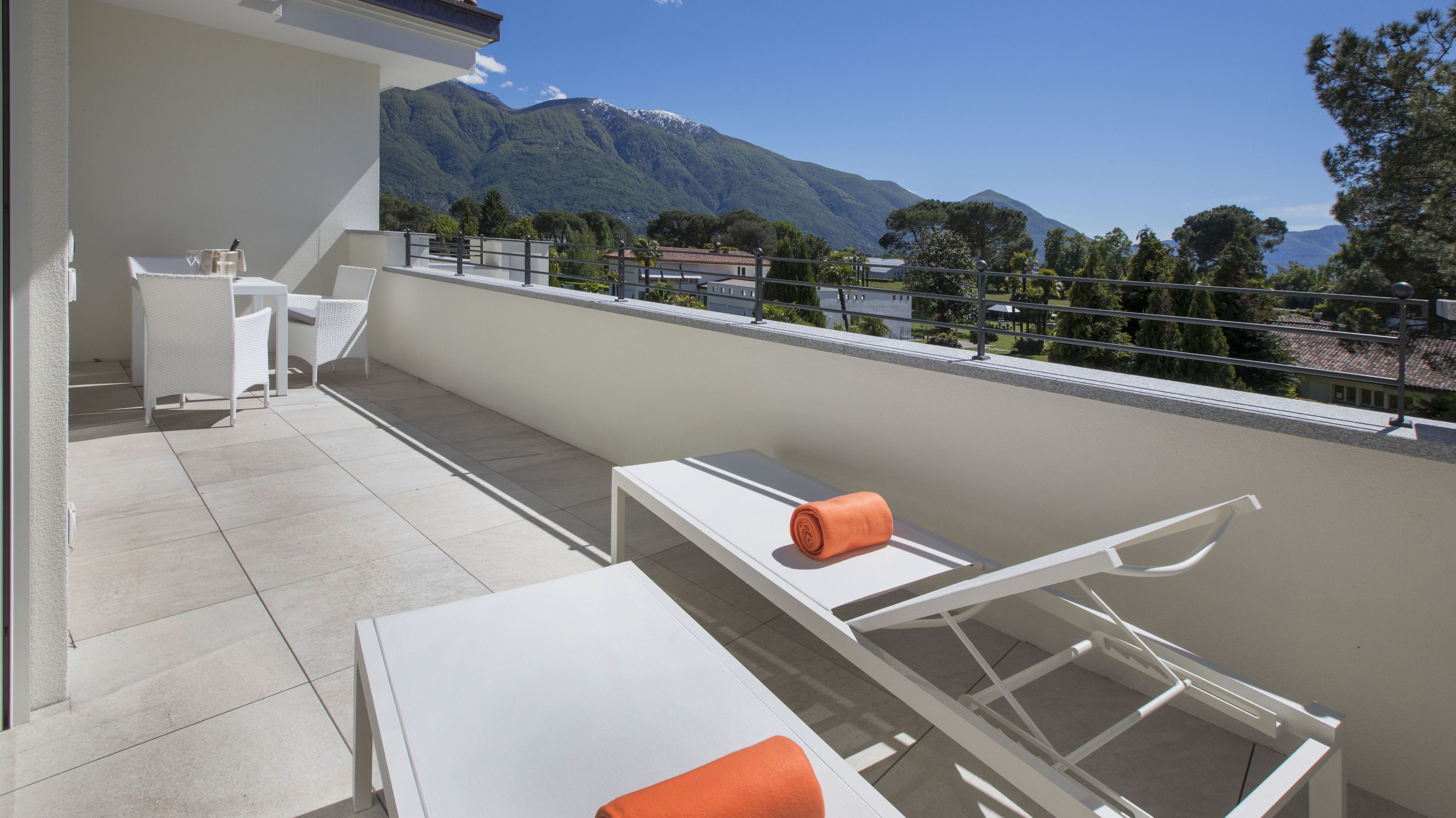 Un balcon avec une table blanche, des chaises et une serviette. On aperçoit une vue sur les montagnes en arrière-plan.