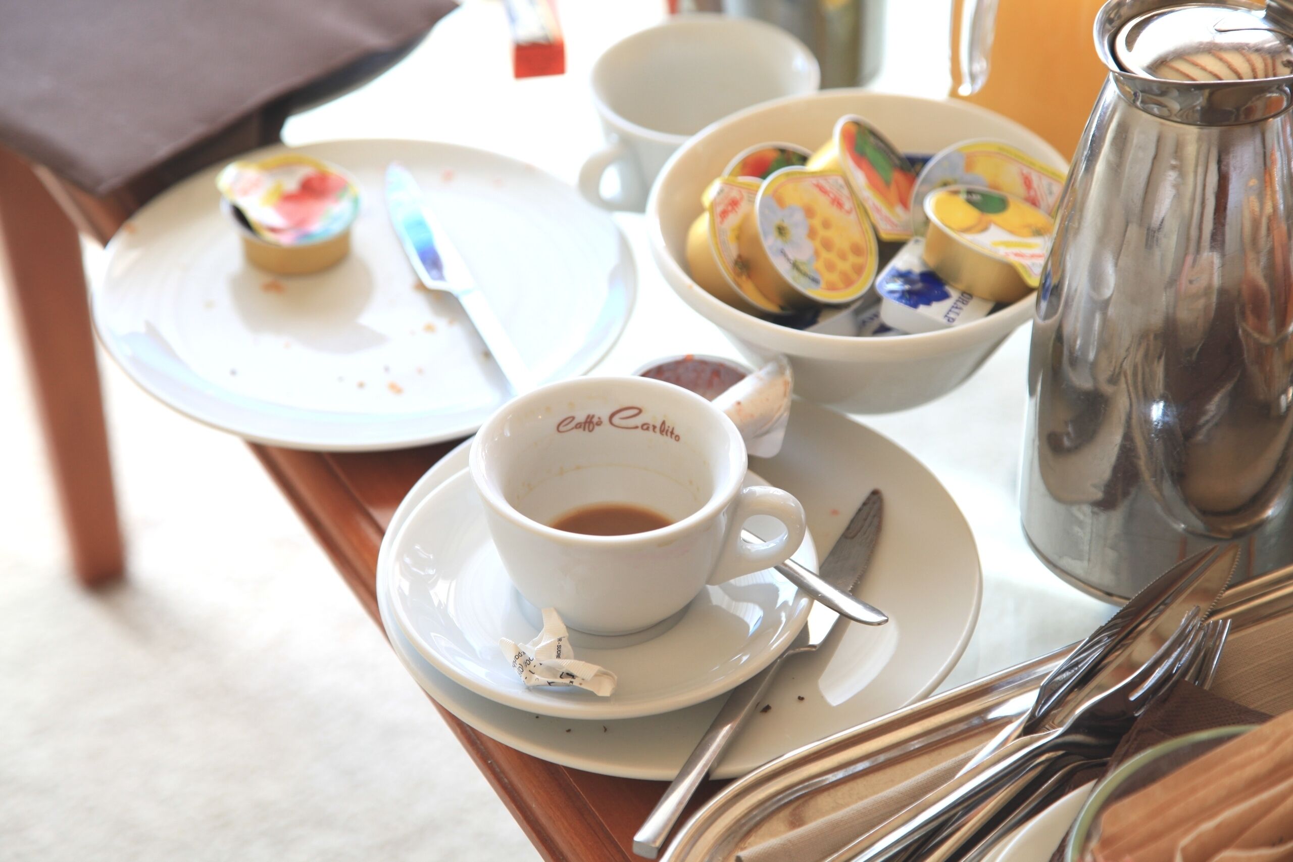 A table with a cup of coffee, a bowl of fruit, a teapot, and a plate with a pastry.
