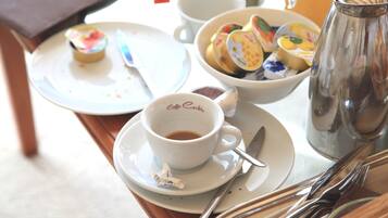 A table with a cup of coffee, a bowl of fruit, a teapot, and a plate with a pastry.