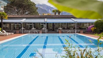 Une piscine avec une terrasse carrelée, un espace de détente couvert avec des tables et des chaises, et une vue imprenable sur les montagnes.
