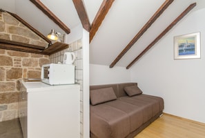 A room with a stone wall, wooden beams, a white appliance, a brown sofa, and a framed picture. - Villa Desideria (Split)