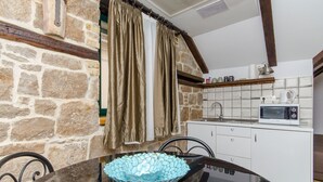 A stone wall, a kitchen with a microwave, and a dining table with a blue glass bowl. - Villa Desideria (Split)