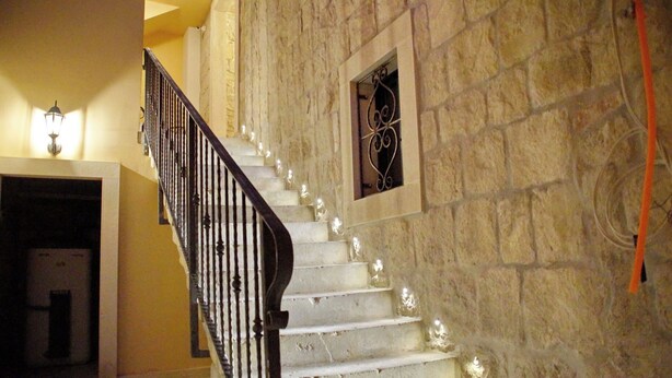 A staircase with white steps and a black railing, leading to a room with a stone wall and a decorative iron window. - Villa Desideria (Split)