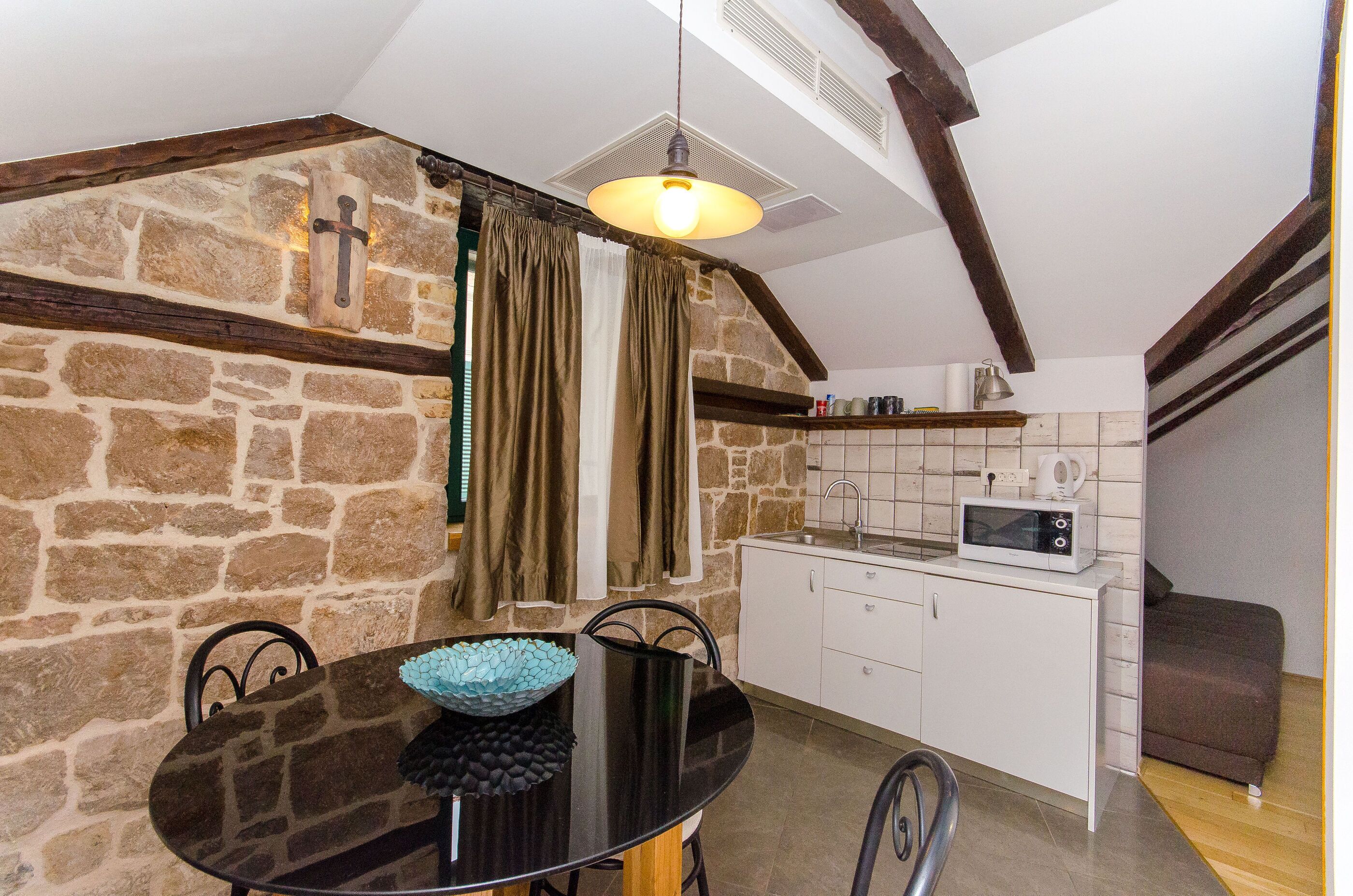A kitchen with a stone wall, a microwave, and a dining area with a black table and chairs.