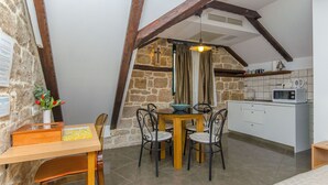 A dining area with a table and chairs, a kitchen with a microwave, and a stone wall with a cross. - Villa Desideria (Split)