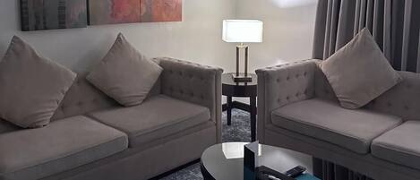 A hotel room with two sofas, a coffee table, a lamp, and a large abstract painting on the wall.