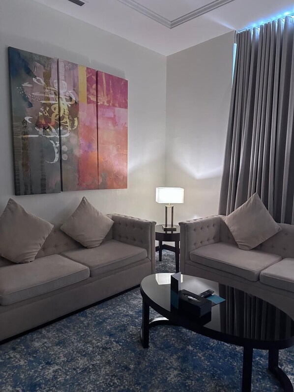 Habitación de hotel con dos sofás, una mesita de centro, una lámpara y un cuadro abstracto grande en la pared.