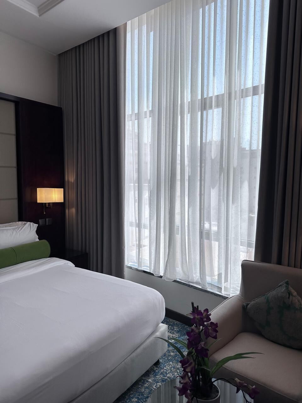 A hotel room with a bed, a sofa, a lamp, and a window with curtains.