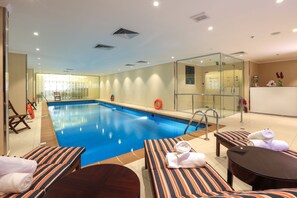 Un espace piscine d’hôtel comprenant des chaises longues, une table et un espace douche fermé par des parois de verre.