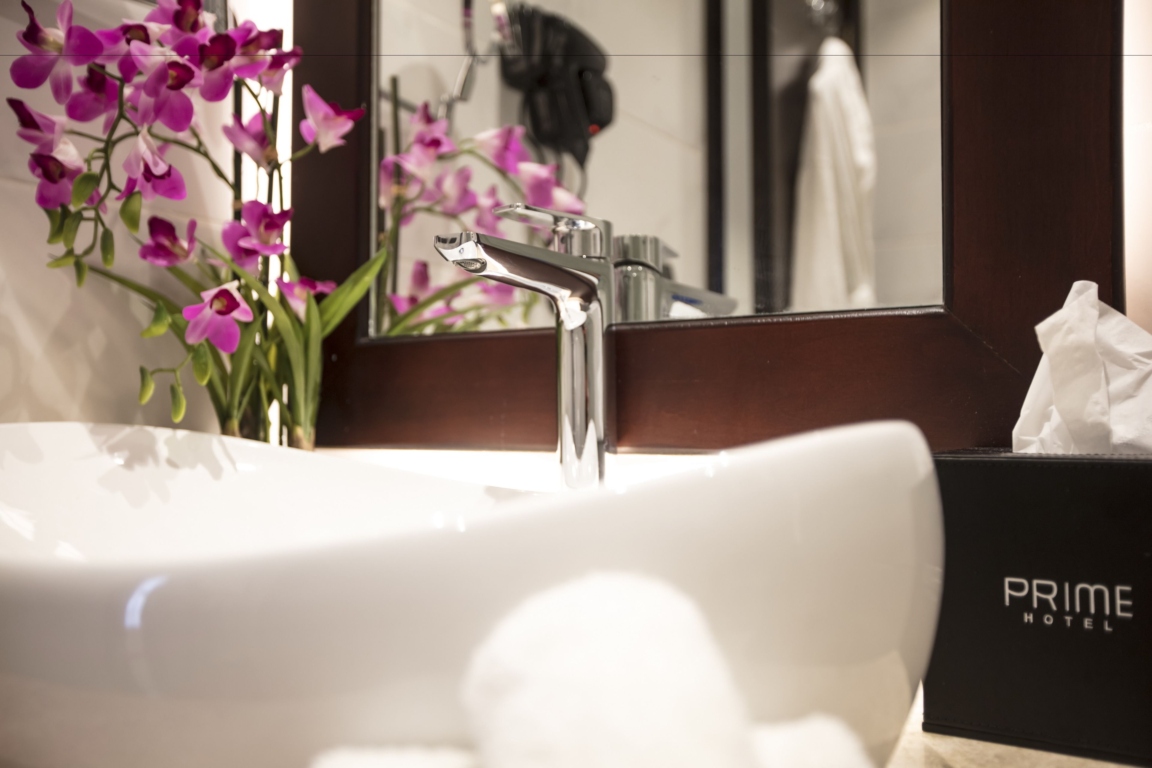 A bathroom with a white sink, a mirror, and a bouquet of pink orchids.