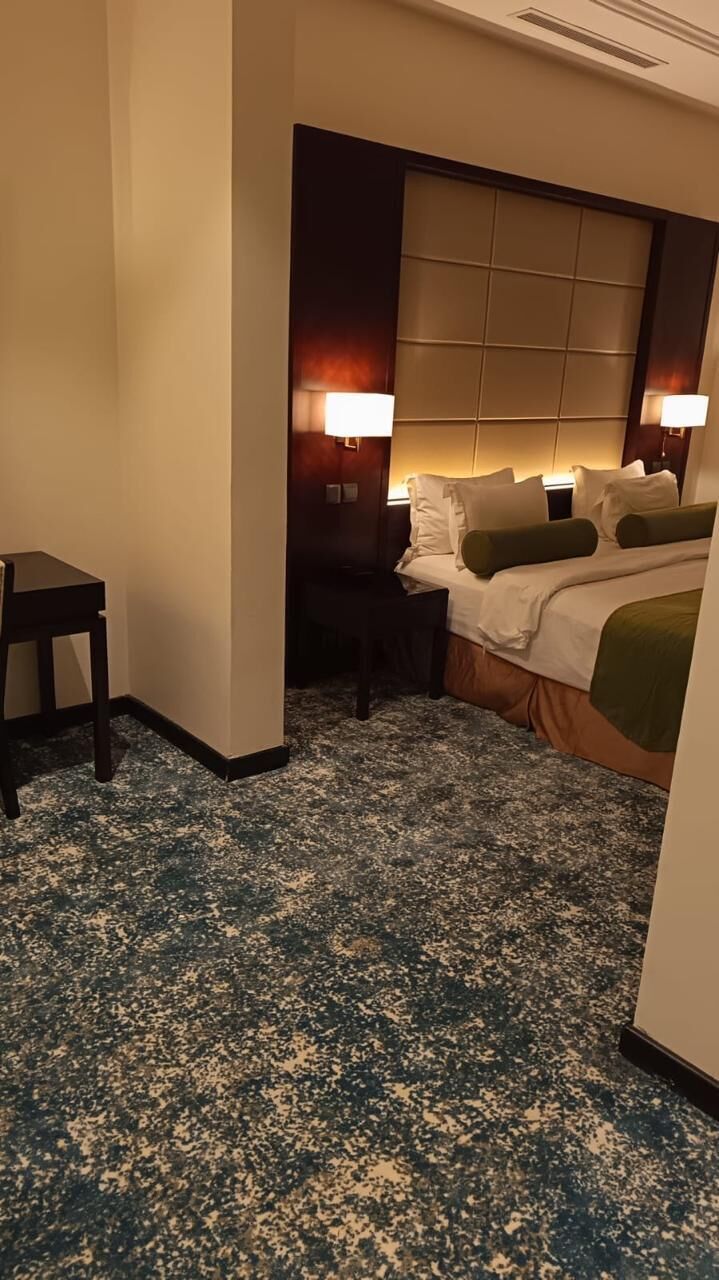 Una camera d'albergo con un letto, comodini, una scrivania e un pavimento rivestito di moquette.