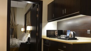 Een hotelkamer met een bed, nachtkastje, bureau met een computer, magnetron, waterkoker en een waterfles.