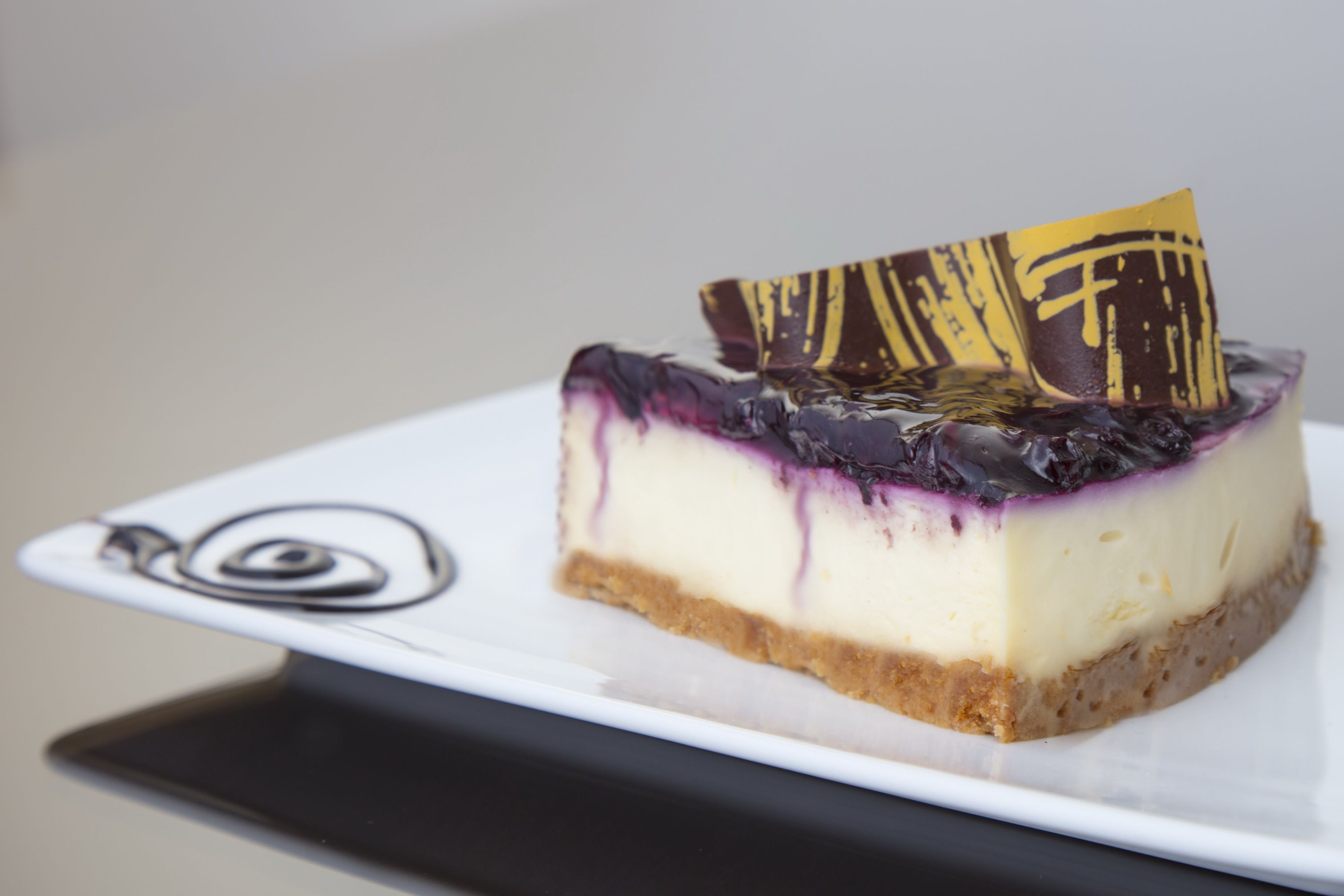 Una fetta di cheesecake con un pezzo di cioccolato decorativo su un piatto bianco.