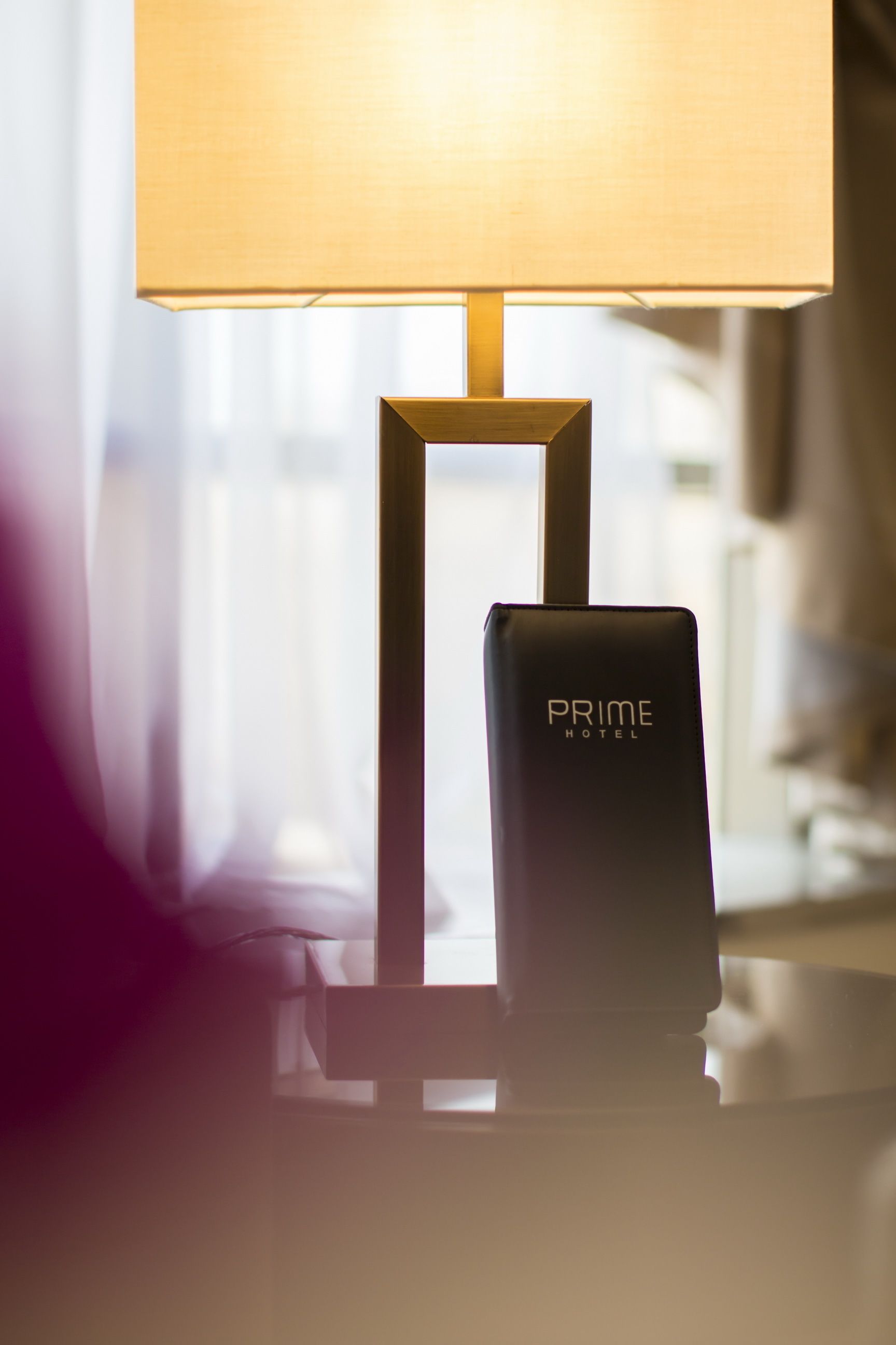 A lamp with a rectangular base and a square shade, placed on a table next to a device labeled "PRIME HOTEL".