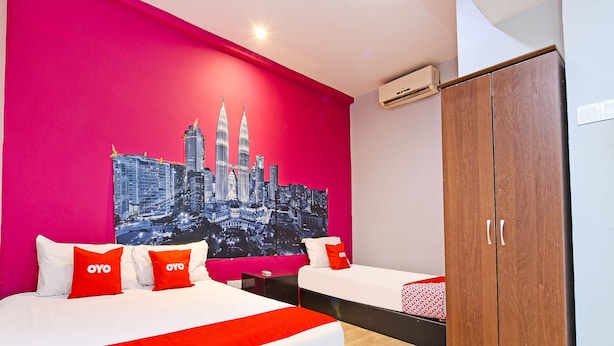 Ein Hotelzimmer mit einer lebhaften rosa Wand, einem großen Bett mit weißer und roter Bettwäsche, einem hölzernen Kleiderschrank und einem Stadtbildgemälde.