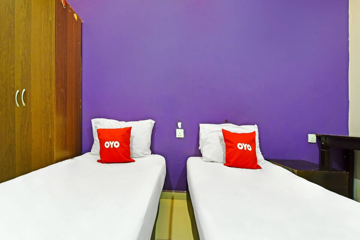 Two single beds with white bedding and red pillows, a wooden wardrobe, and a purple wall.