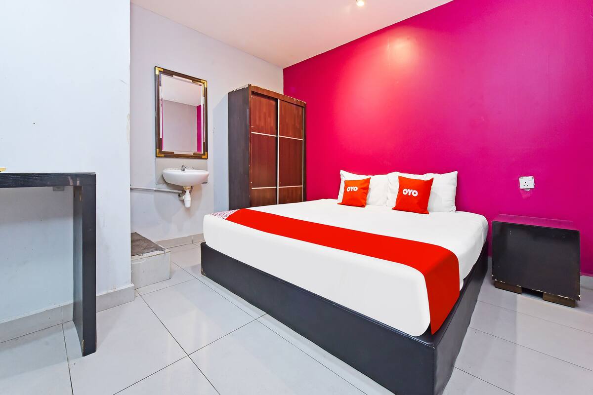 A hotel room with a bed, a bedside table, a mirror, a sink, and a wardrobe.