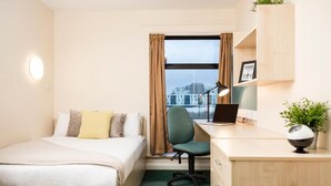 A hotel room with a bed, desk, chair, and a view of the city through the window. - Bonington Student Village - Campus Accommodation (Loughborough)