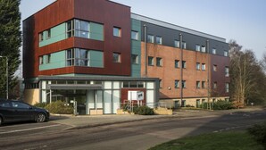 A modern building with a mix of brick and metal exterior, large windows, and a parking lot. - Bonington Student Village - Campus Accommodation (Loughborough)