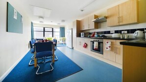 A modern kitchen with wooden cabinets, a stove, and a dining area with blue chairs. - Bonington Student Village - Campus Accommodation (Loughborough)