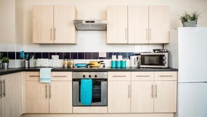 A kitchen with light wooden cabinets, a stove, a microwave, and a refrigerator. - Bonington Student Village - Campus Accommodation (Loughborough)
