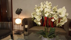 A living room with a glass coffee table, a potted orchid, a sofa, and a floor lamp. - ELEVEN'S Hôtel & Spa (Abidjan)