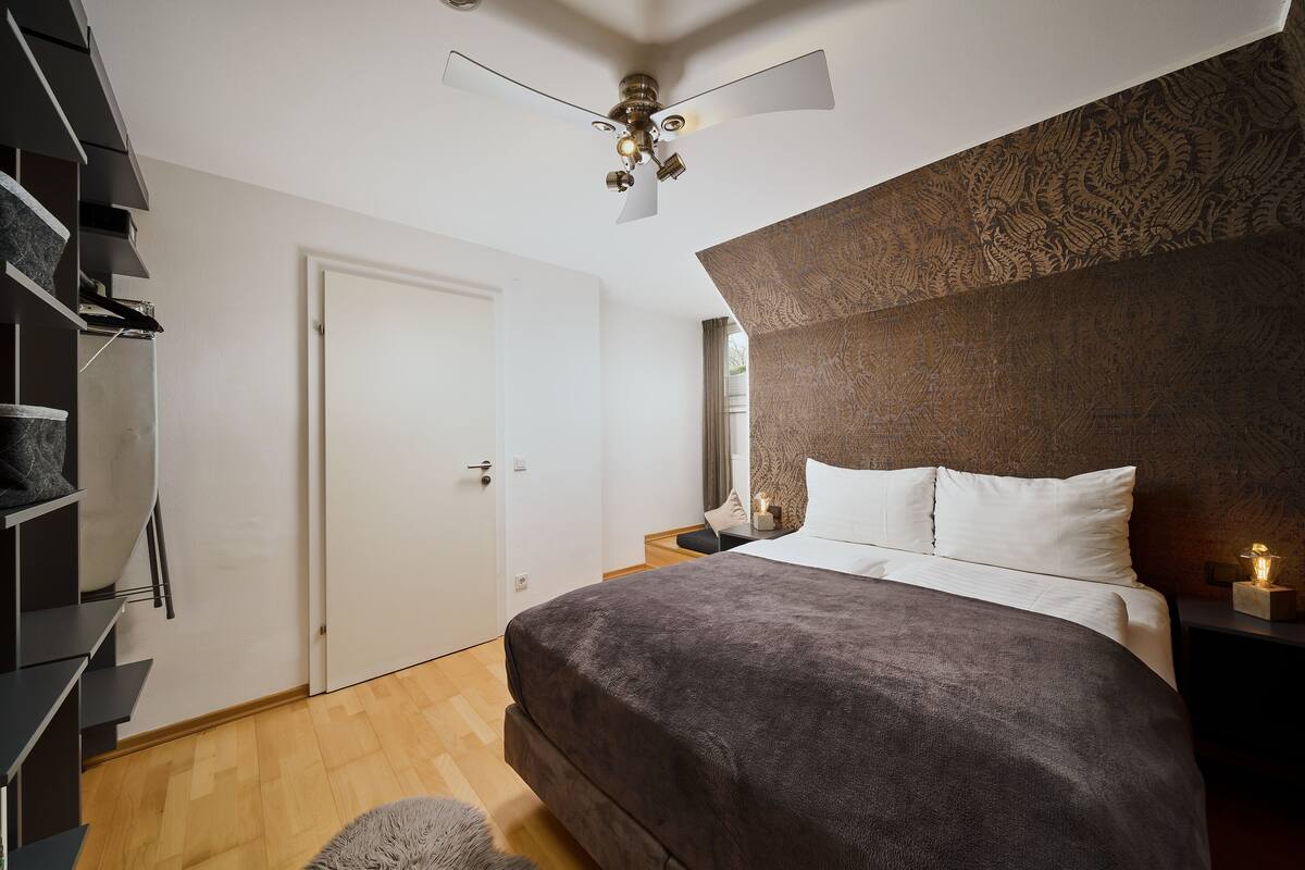 A bedroom with a bed, a ceiling fan, a nightstand, and a wardrobe.