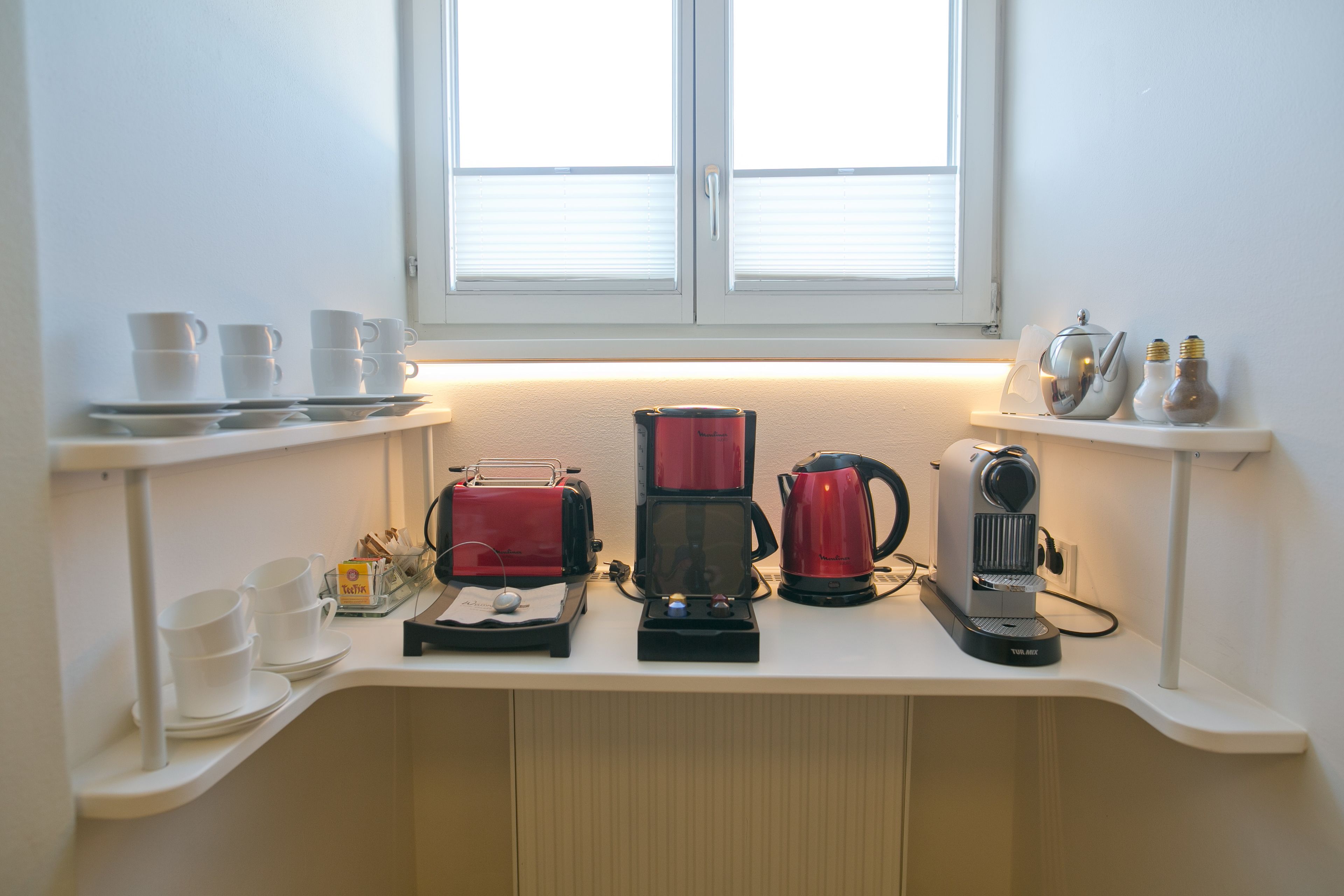 A kitchen counter with a coffee maker, a toaster, and a kettle. There are cups and a tray on the counter.