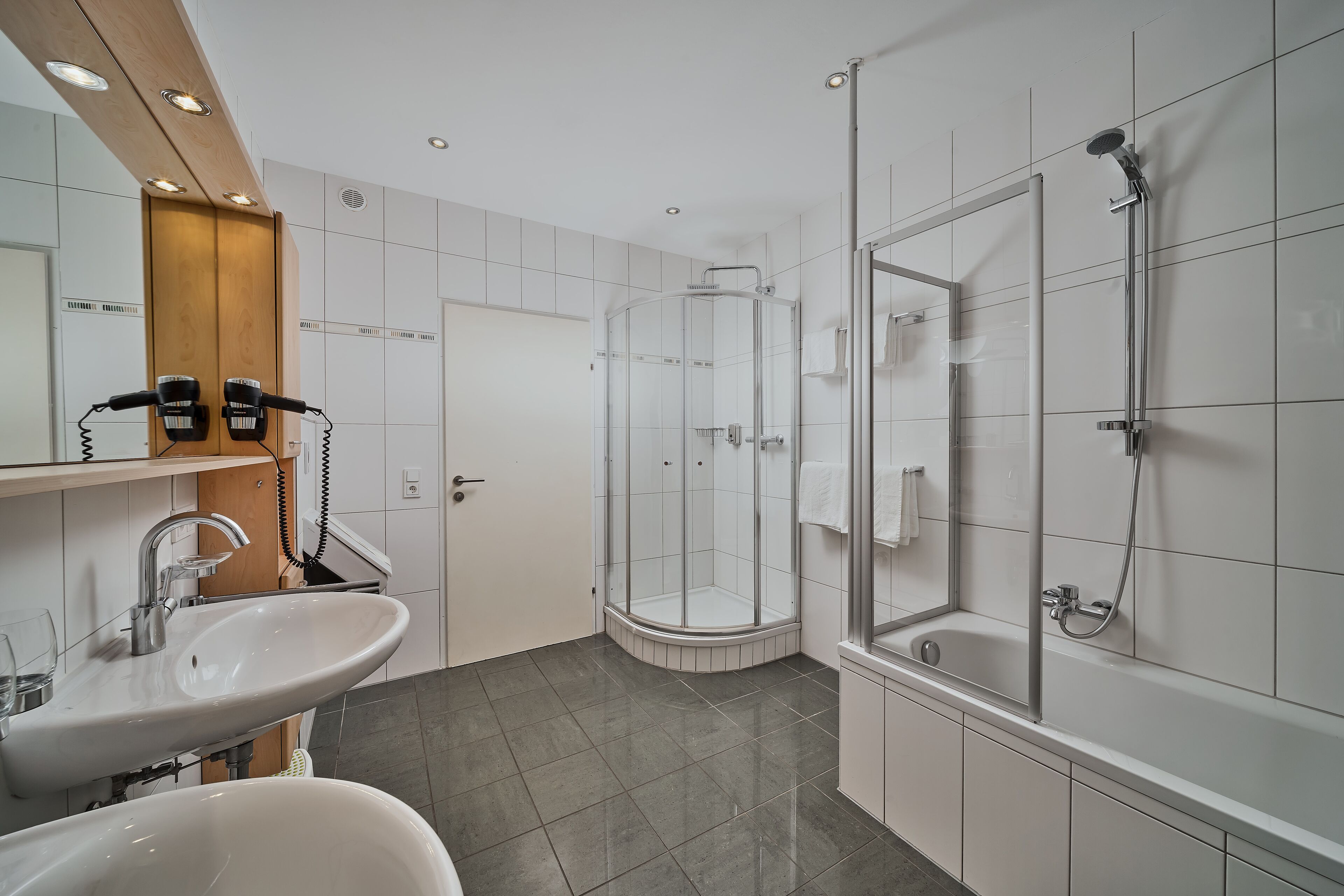 Une salle de bain moderne dotée d’un grand lavabo, d’une douche et d’une cabine de douche en verre.